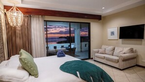 Una camera da letto con un letto, un cuscino verde, un cuscino bianco, una coperta verde, un divano beige e una TV appesa al muro.