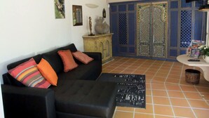 A living room with a black sofa, colorful cushions, a small cabinet, a TV, and a decorative wall panel. - Domaine les Flachères (14pers) (Dieulefit)