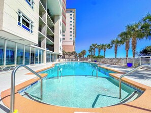 A swimming pool with a clear blue water, surrounded by a white building with balconies, and palm trees in the background. - South Shore Villas 503 (North Myrtle Beach)