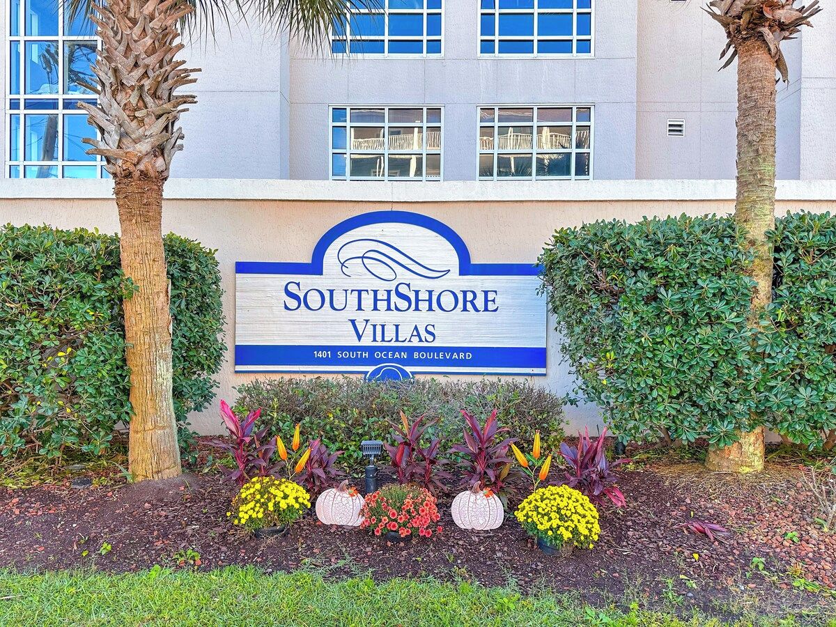 Un letrero de SouthShore Villas con una vista clara de la fachada del edificio y un jardín ajardinado.