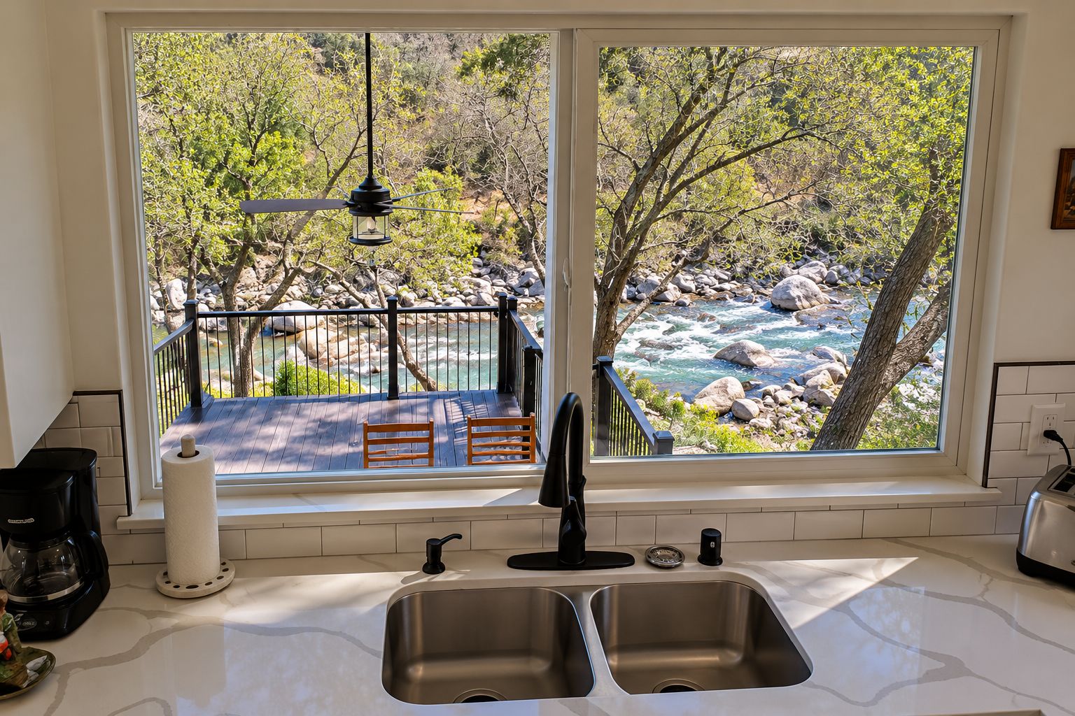 Una cocina con un ventanal que da a un río pedregoso y árboles.