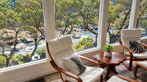Une pièce avec vue sur une rivière et des arbres, meublée avec deux chaises et une petite table sur laquelle est posée une plante.