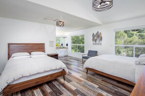 Une chambre avec deux lits, un plancher en bois, une grande fenêtre et un luminaire au plafond.