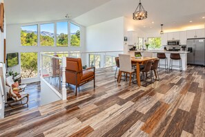 Une cuisine spacieuse équipée d’appareils modernes, un coin repas avec une table et des chaises en bois, et un balcon offrant une vue sur les montagnes.