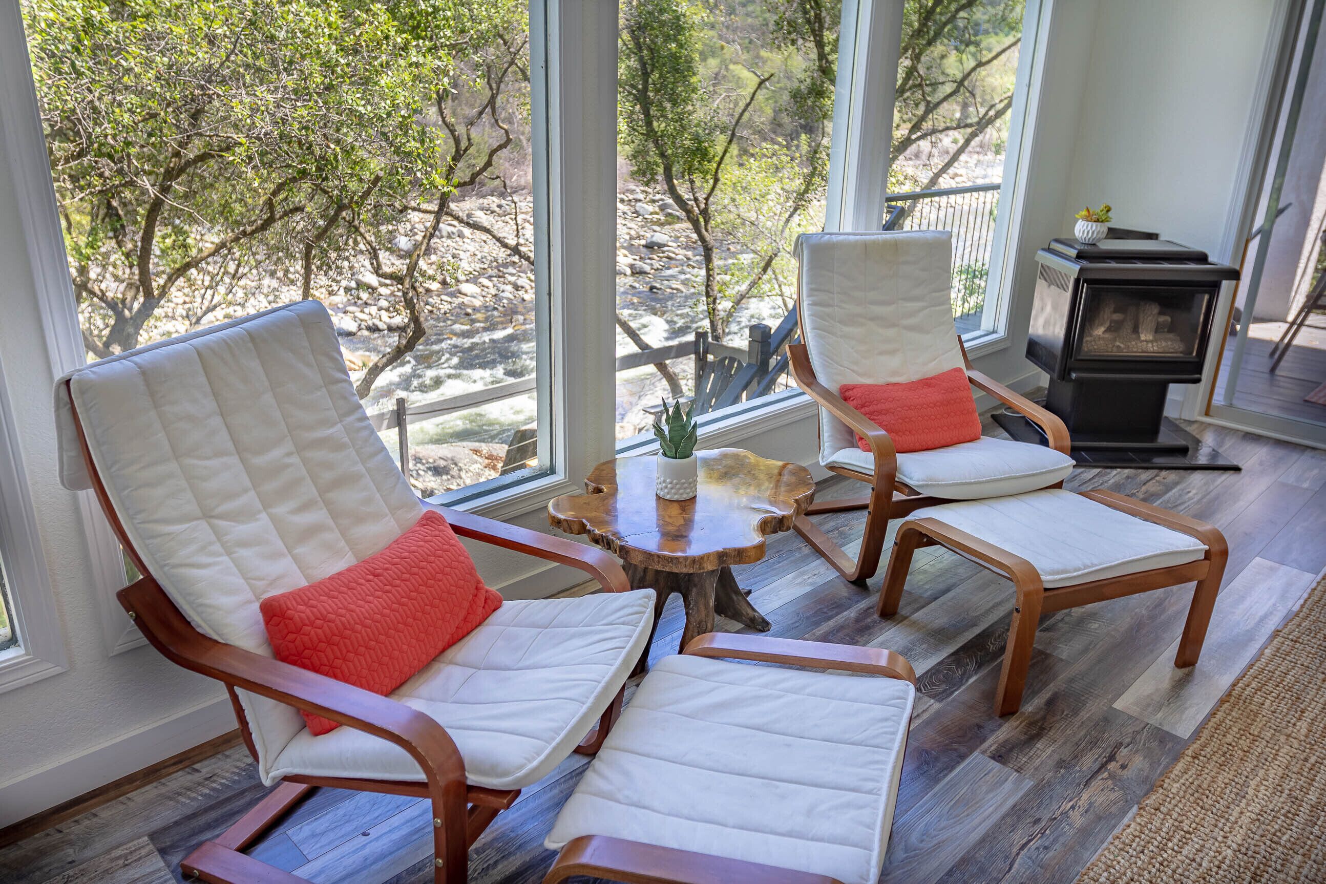 Une pièce comprenant deux fauteuils blancs avec des coussins rouges, une petite table en bois sur laquelle est posée une plante, et une cheminée.