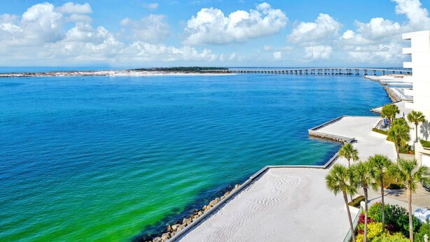 A coastal view with a pier extending into the sea, a sandy beach, and a white building with palm trees.