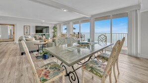 A spacious dining area with a long table, floral-patterned chairs, and a view of the sky through large windows.