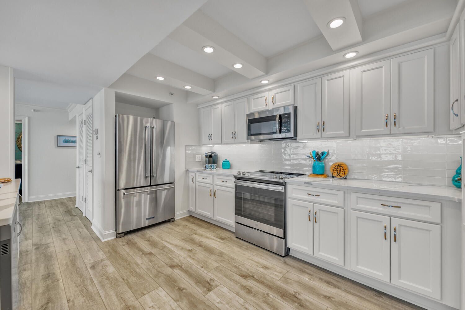 A modern kitchen with white cabinetry, stainless steel appliances, and a wooden floor.