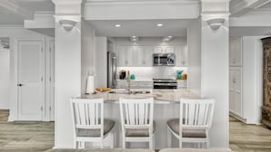 A modern kitchen with white cabinetry, a central island with bar stools, and a stainless steel refrigerator.