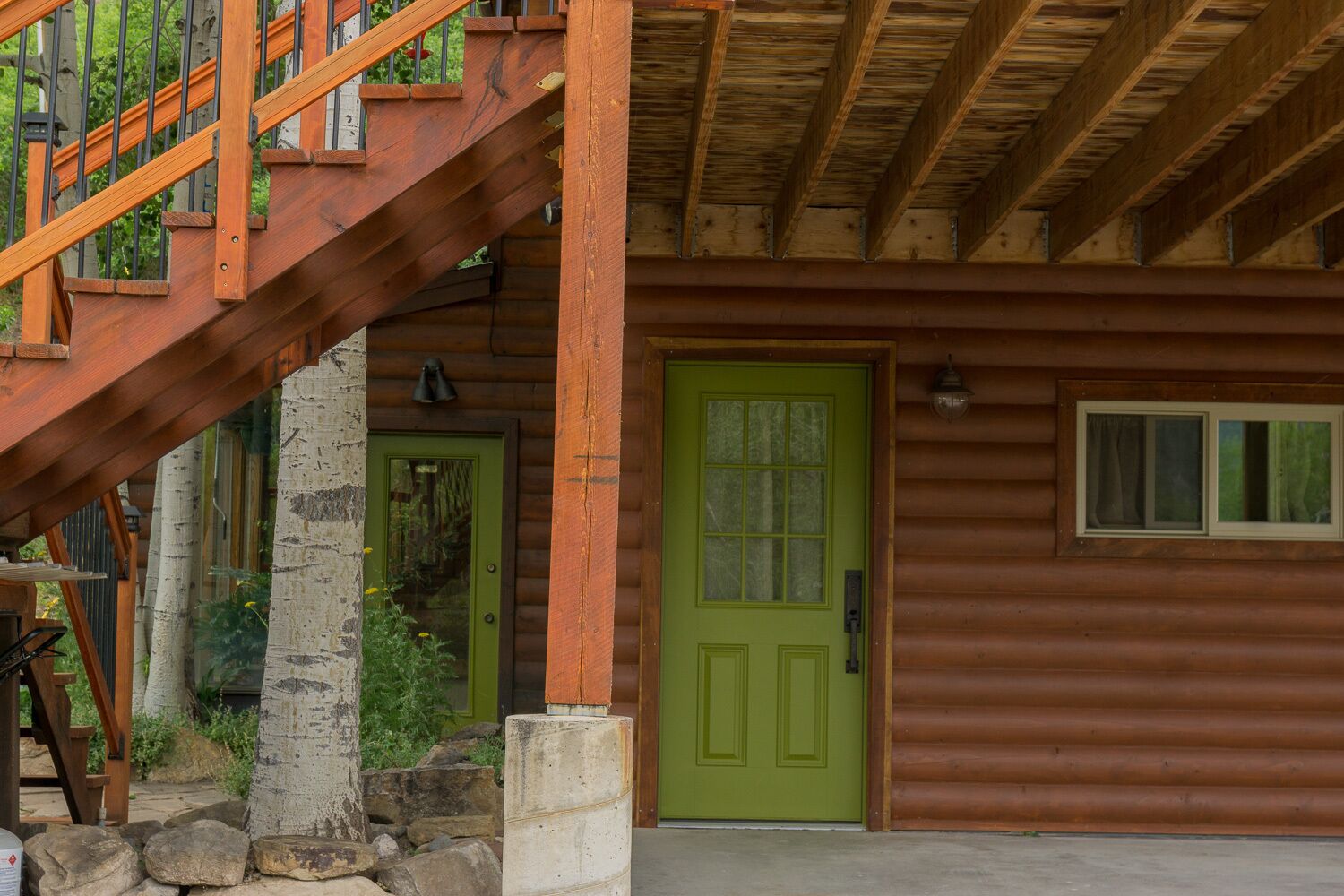 Une cabane rustique en rondins de bois, avec une porte verte, un escalier en bois et des fondations en pierre.