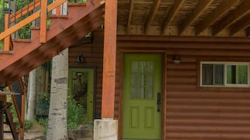 Une cabane rustique en rondins de bois, avec une porte verte, un escalier en bois et des fondations en pierre.