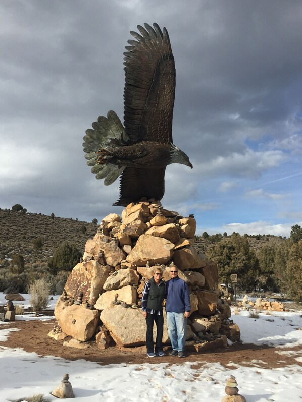 Una escultura de un águila posada sobre una formación rocosa, con dos personas de pie a su lado.