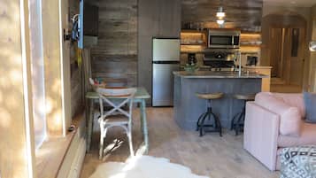 Une cuisine moderne dotée d’un îlot central, un coin repas avec une table et des chaises en bois, et un espace de vie chaleureux avec un canapé et un tapis à motifs.