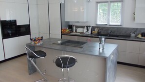 Una cocina moderna con armarios blancos, una isla central con taburetes, un horno negro y una ventana con persianas.