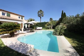 A swimming pool with a curved edge, surrounded by a well-maintained lawn and various plants.