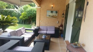 Un área de estar al aire libre con mobiliario de mimbre, una mesa de centro de vidrio y una mesa pequeña con una planta en maceta.