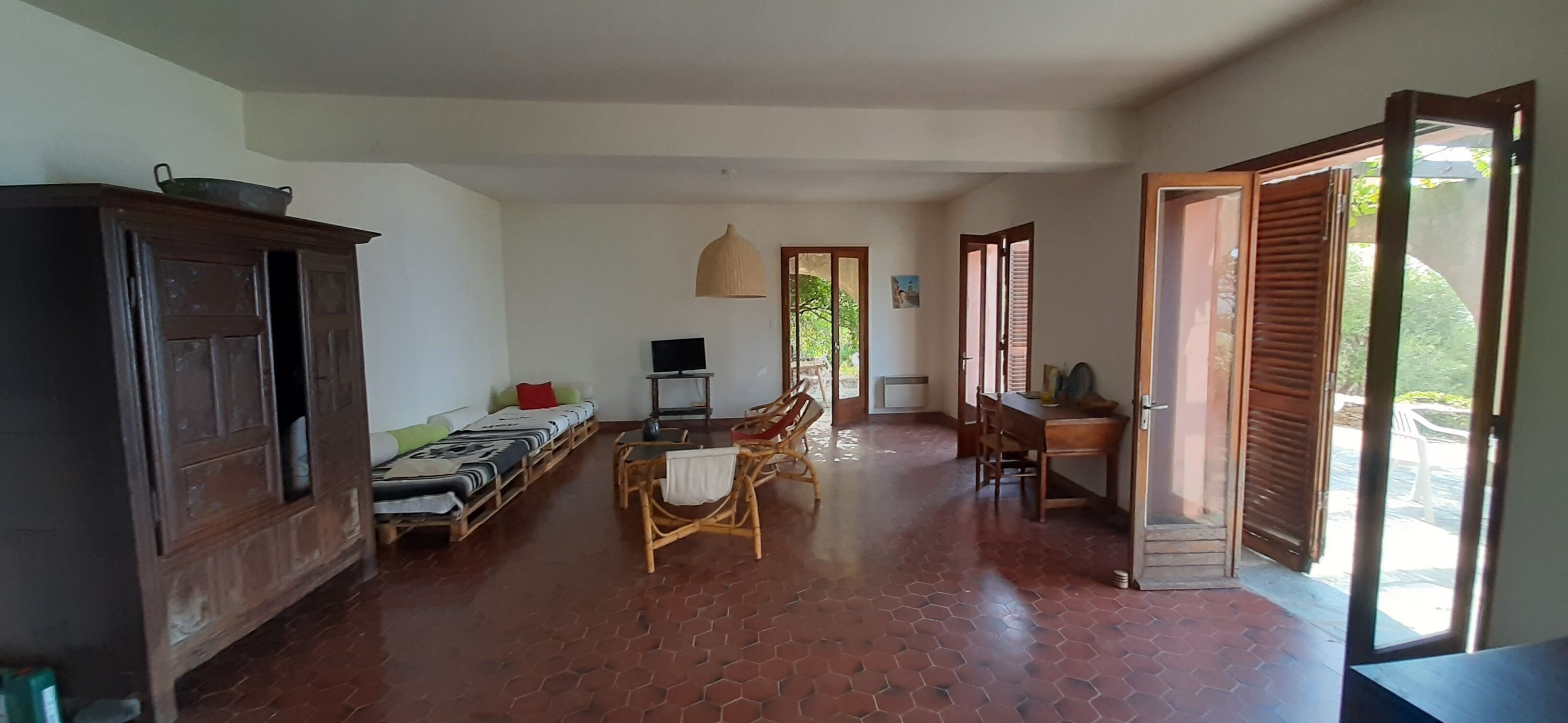 Une pièce spacieuse avec un sol carrelé, un meuble en bois, un ensemble de canapés, une table à manger avec des chaises et un téléviseur.