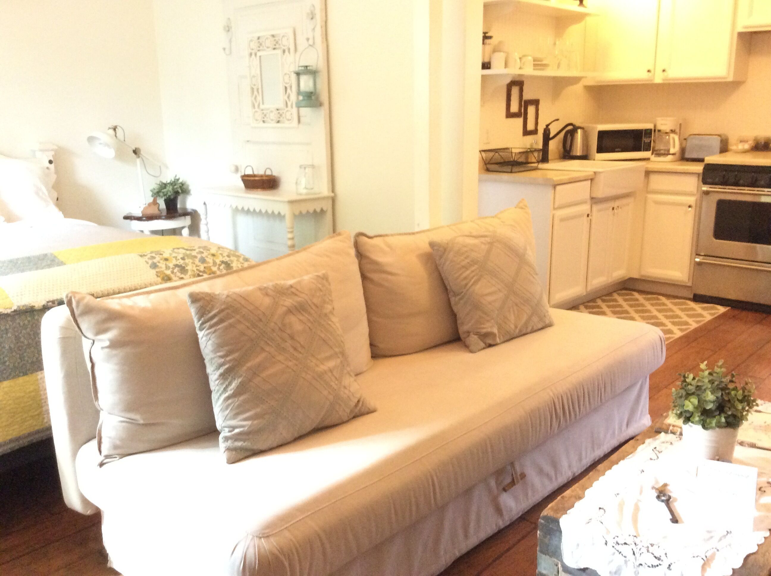 A living room with a beige sofa, a small coffee table, and a kitchen area with white cabinets and appliances.