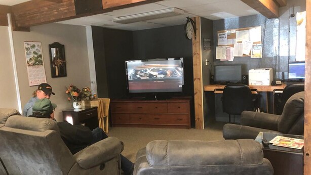 A living room with a television, two recliners, a wooden cabinet, and a desk with a computer. - Campbell Lodge (Glasgow)