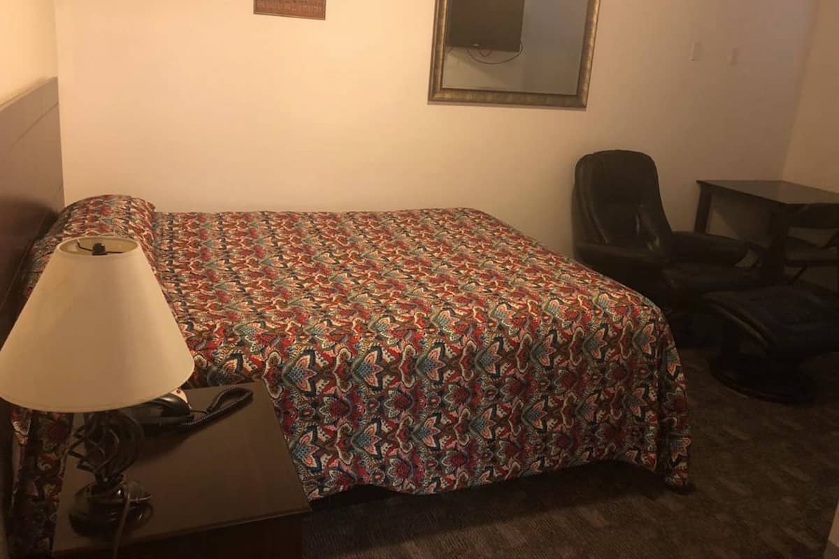 A small, neatly arranged room with a bed, a chair, a desk, and a lamp.