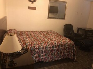 Una habitación pequeña y ordenada con cama, una silla, escritorio y lámpara.