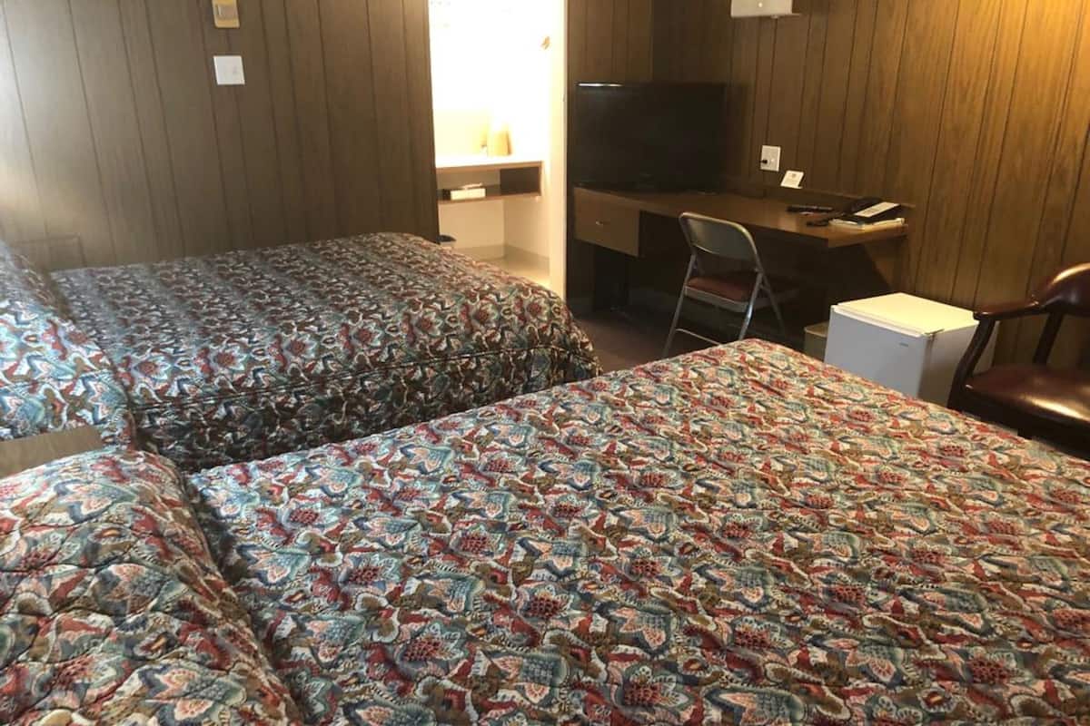 A hotel room with two beds, a desk, a chair, and a television.