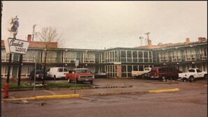 A motel with a sign reading "Campbell Lodge," featuring a row of parked vehicles and a building with large windows. - Campbell Lodge (Glasgow)