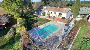Une villa blanche avec un toit en tuiles, une piscine et un jardin agrémenté de divers arbres et arbustes.
