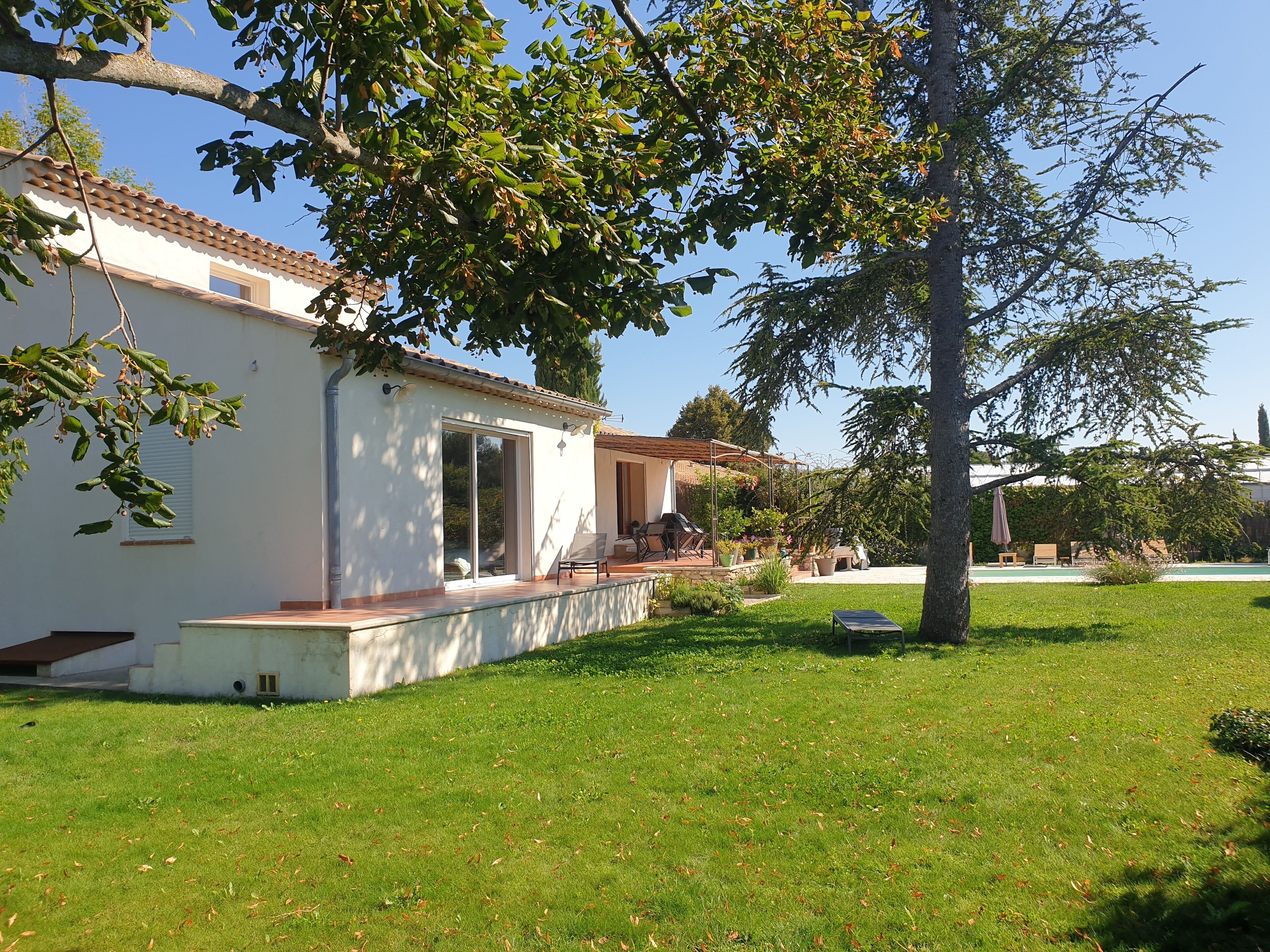 Un bâtiment blanc avec un toit en tuiles, un patio couvert et une pelouse verdoyante.
