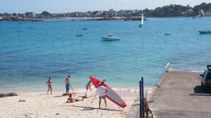Una playa con gente, una tabla de surf y barcos en el agua.