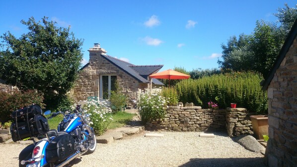 A stone house with a gravel driveway, a parked motorcycle, and a red umbrella.