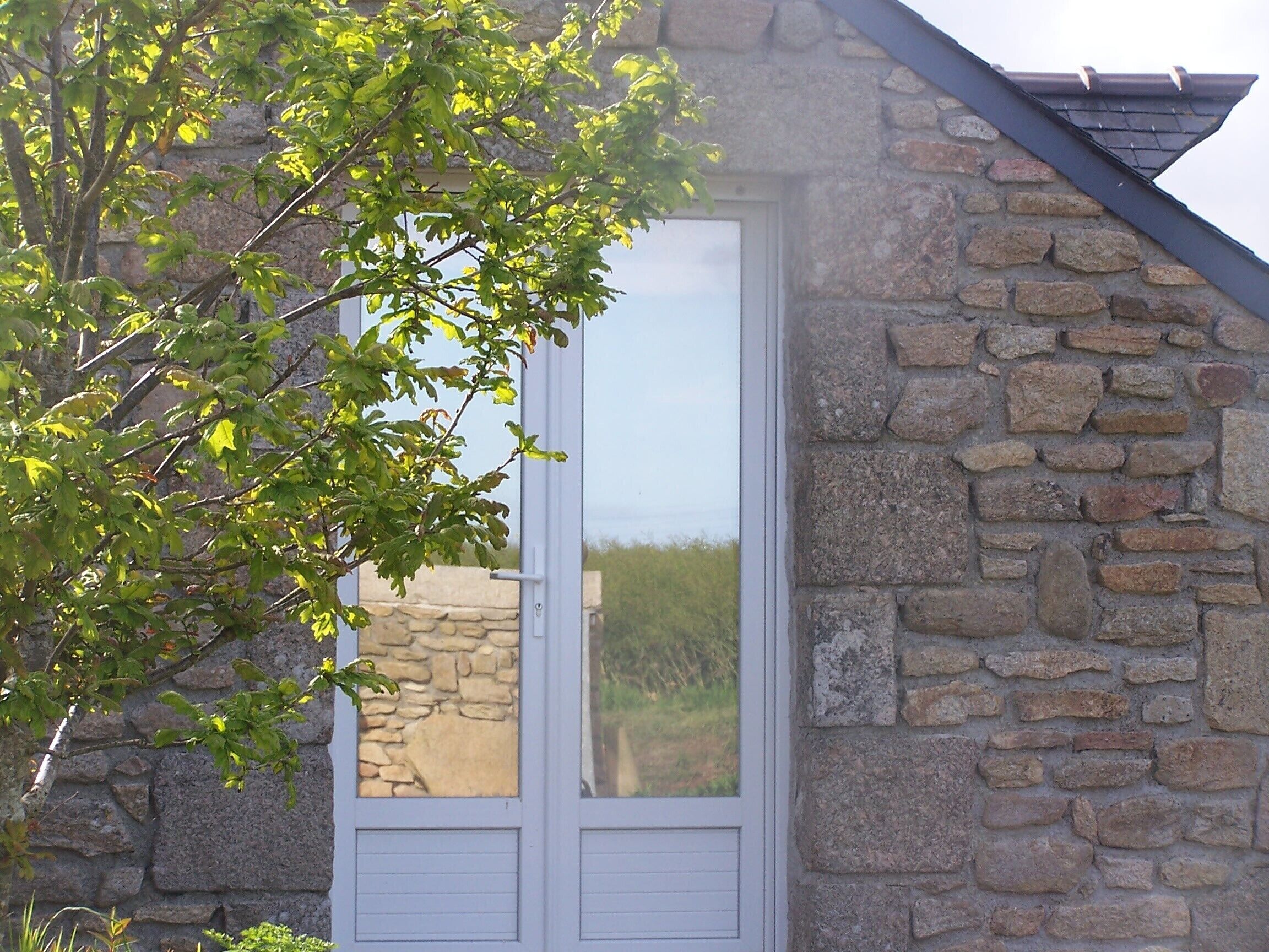 Un edificio de piedra con puerta blanca y ventana, rodeado de vegetación.