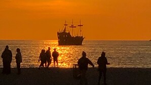 A sunset with silhouettes of people and a ship on the beach.