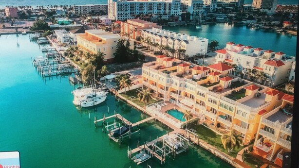 An aerial view of a coastal resort area with multiple buildings, a marina with boats, and a clear view of the ocean.