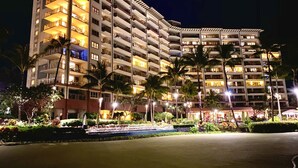 A multi-story hotel with balconies, palm trees, and a well-lit pool area. - Ocean Front Sunset & Whale-Watching Views at Hyatt Vacation Club (Lahaina)