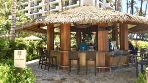 A thatched-roof bar area with seating, a sign for the Wailele Lagoon, and a multi-story building in the background. - Ocean Front Sunset & Whale-Watching Views at Hyatt Vacation Club (Lahaina)