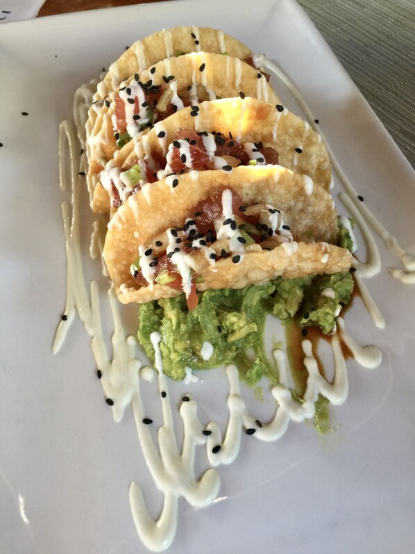 A plate with three tacos, each topped with guacamole, tomatoes, and a white sauce, garnished with black sesame seeds. - Ocean Front Sunset & Whale-Watching Views at Hyatt Vacation Club (Lahaina)
