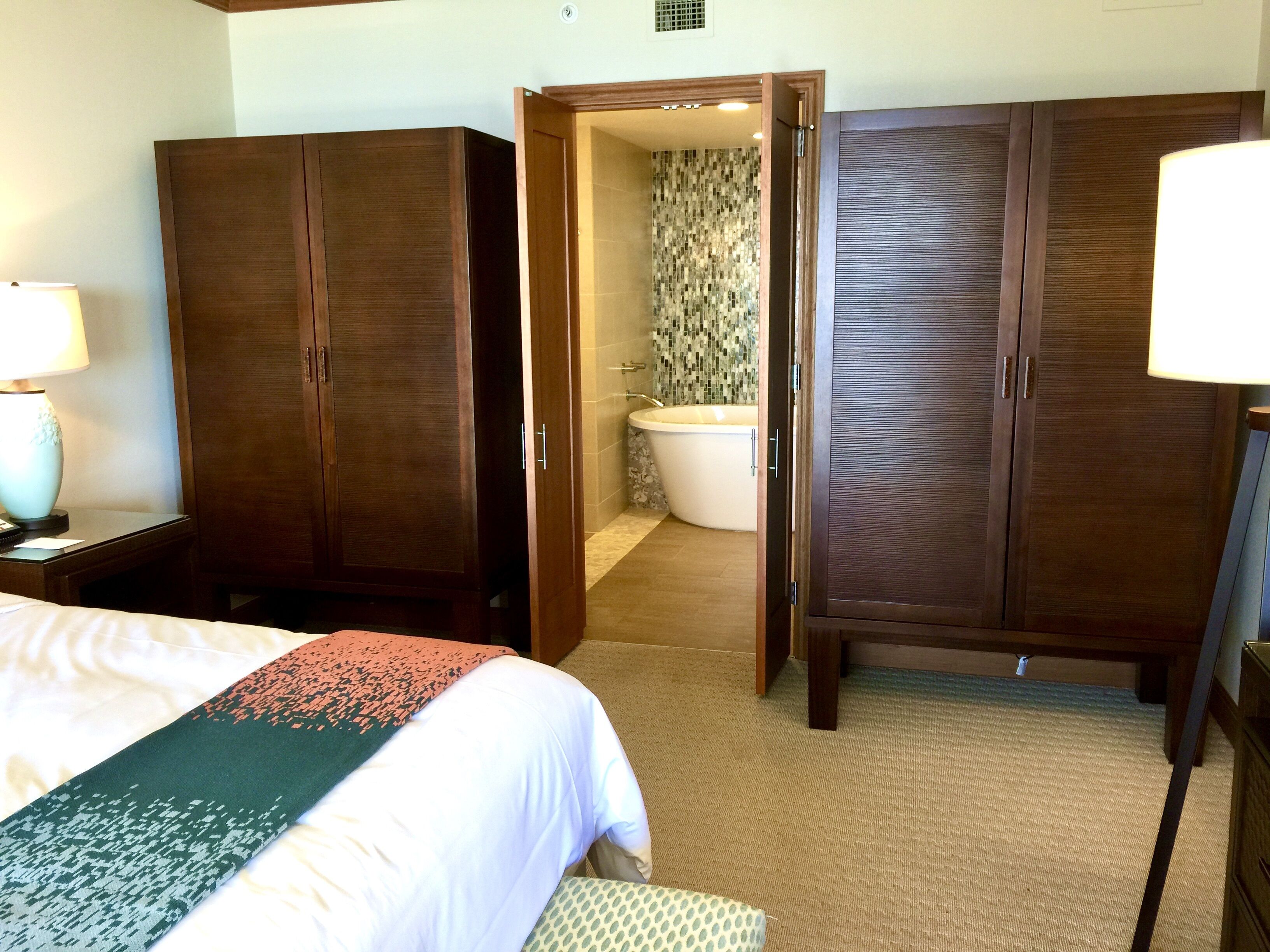 Een hotelkamer met een bed, nachtkastje, bureau, kledingkast en een badkamer met bad en toilet.