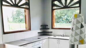 Uma cozinha com bancada de madeira, armários brancos, fogão a gás e duas janelas com molduras decorativas.