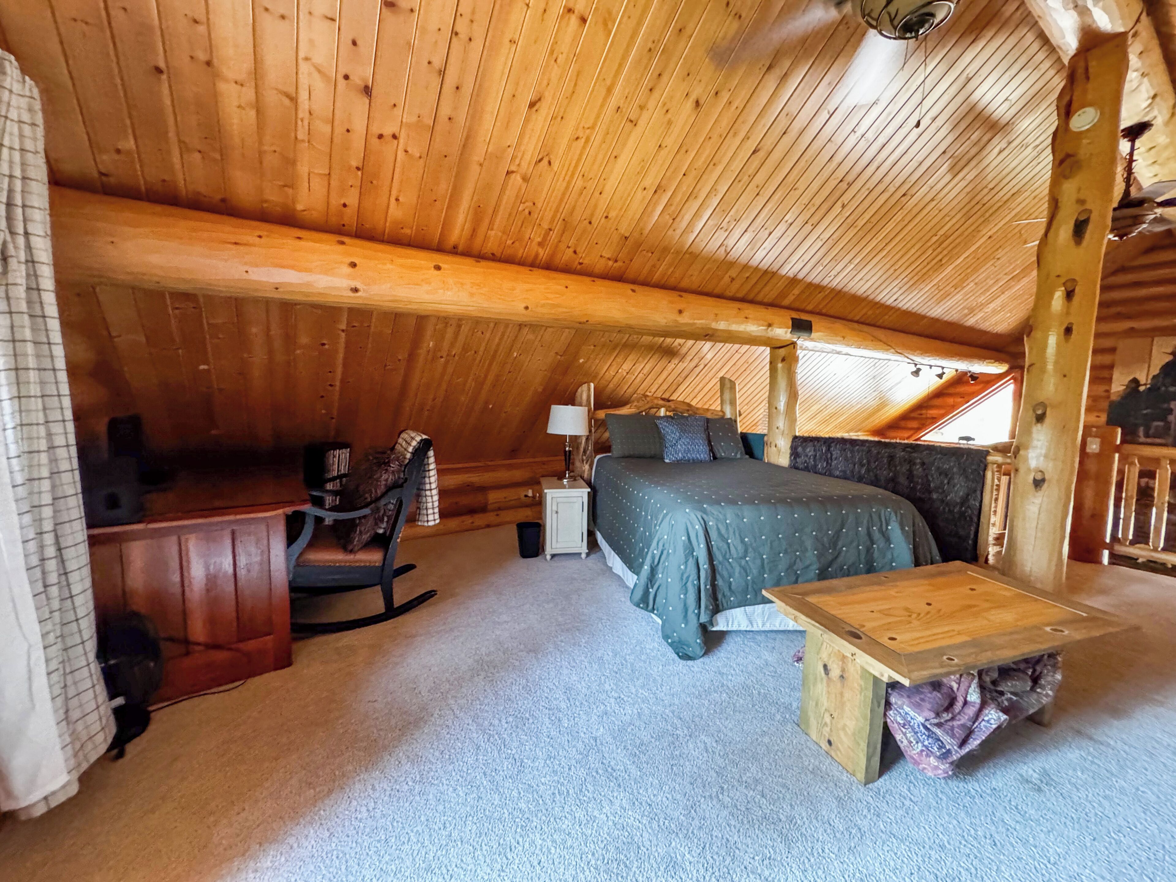 A cozy attic bedroom with a wooden ceiling, a bed, a desk, and a chair.