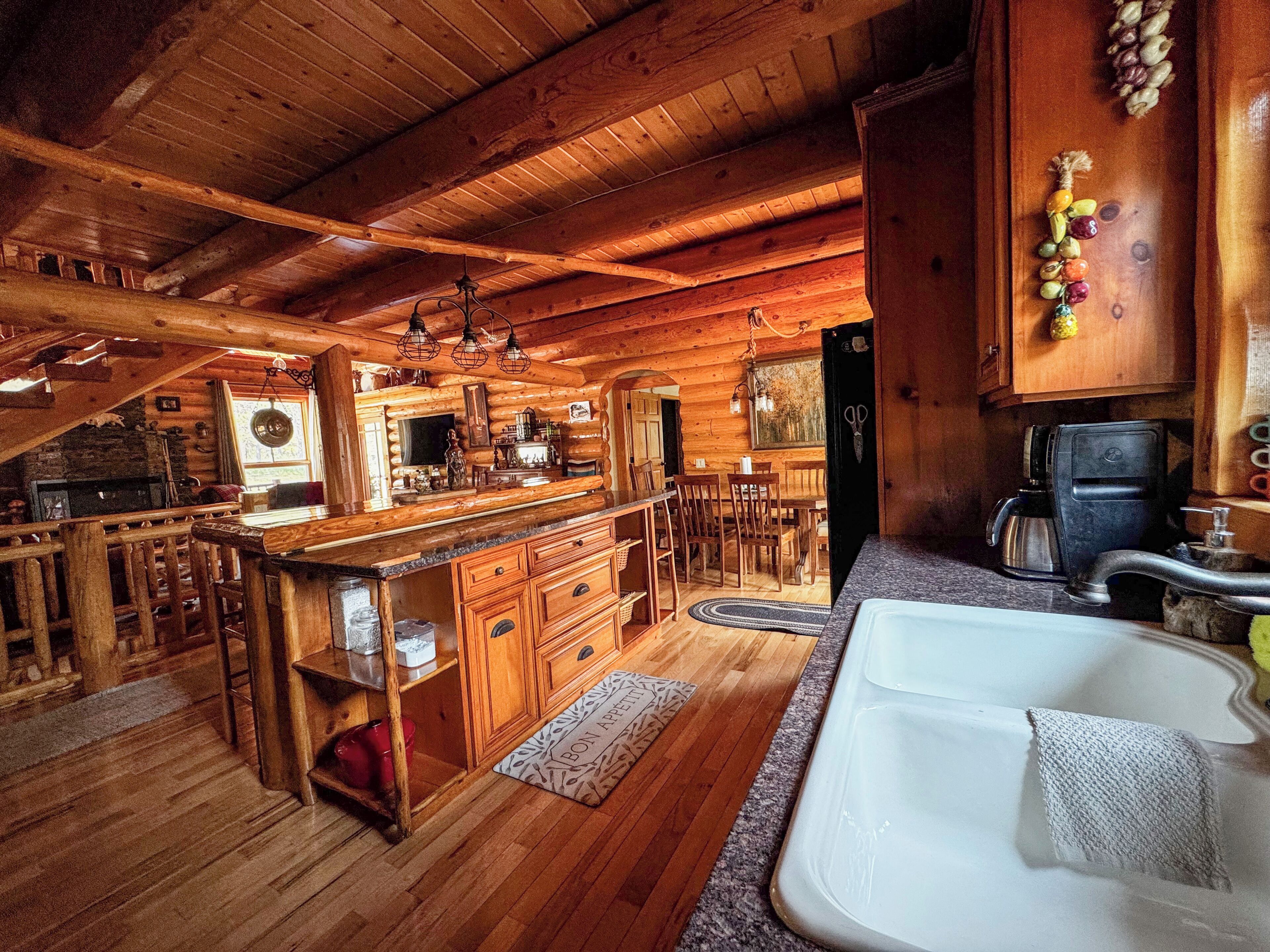 A wooden cabin interior with a kitchen, dining area, and a large window.