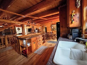A wooden cabin interior with a kitchen, dining area, and a large window.