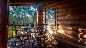 Una cabaña de madera con un balcón, una mesa con sillas y un ventanal con vistas a un bosque.