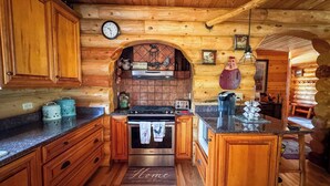 A wooden cabin interior with a kitchen featuring a stove, oven, and a clock on the wall.