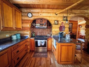 Interior de una cabaña de madera con cocina que incluye estufa, horno y un reloj en la pared.