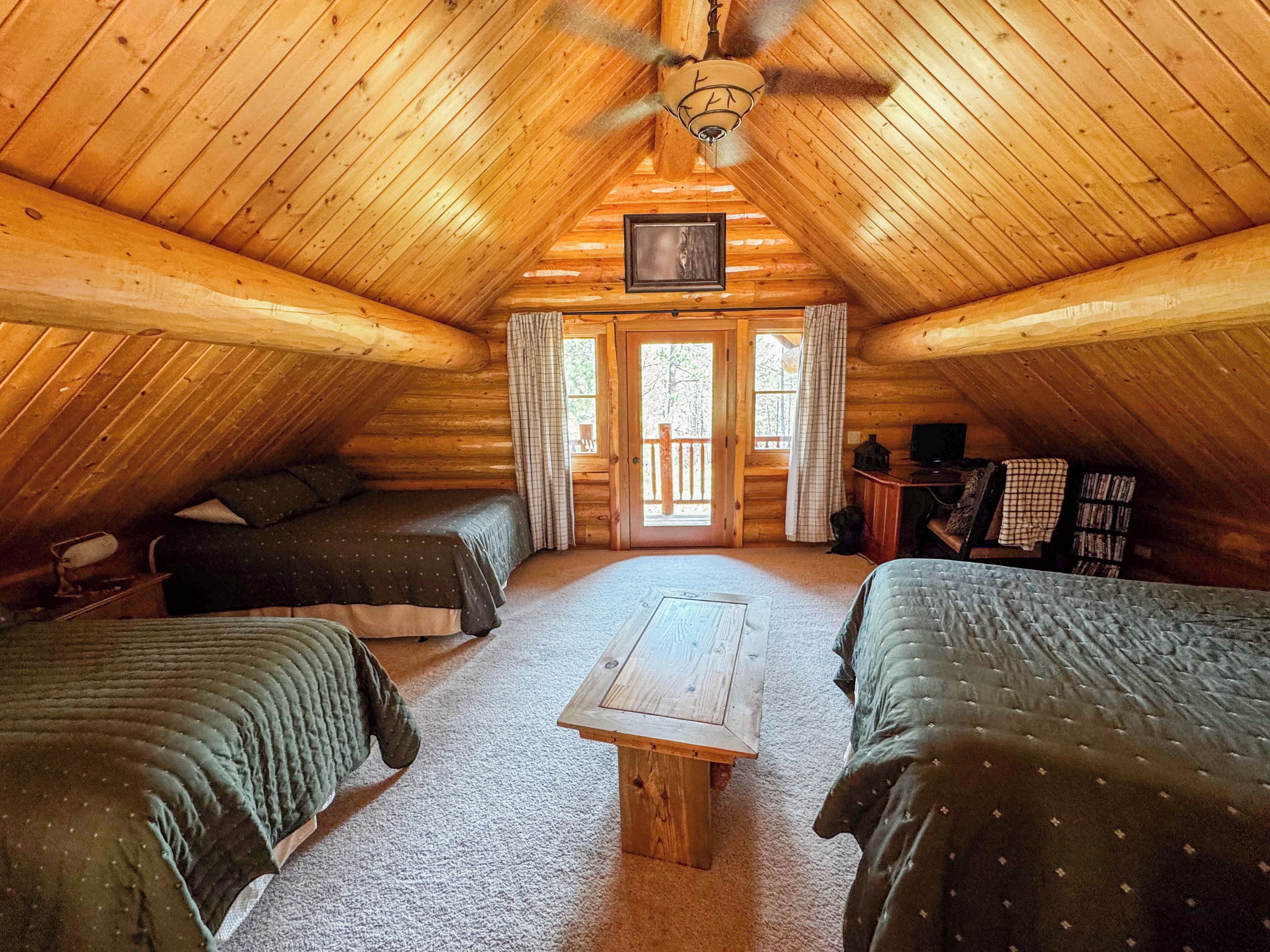 Ein gemütliches Schlafzimmer im Dachgeschoss mit zwei Betten, einem Holztisch und einem Deckenventilator.