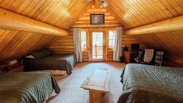 A cozy attic bedroom with two beds, a wooden table, and a ceiling fan.