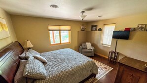 A bedroom with a bed, a desk, a chair, a window, and a ceiling fan.