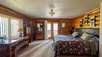 A log cabin bedroom with a bed, dresser, and a desk with a lamp.