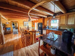 L’intérieur d’un chalet en bois comprend un coin repas, une cuisine et un escalier apparent qui mène à un autre niveau.